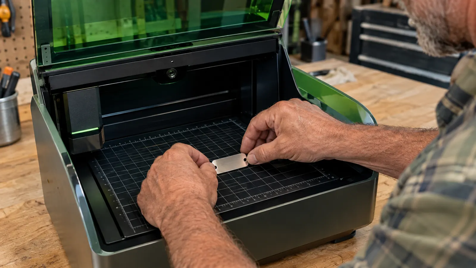 A man's hands placing a small stainless steel tag blank into the open work area of a desktop laser engraver