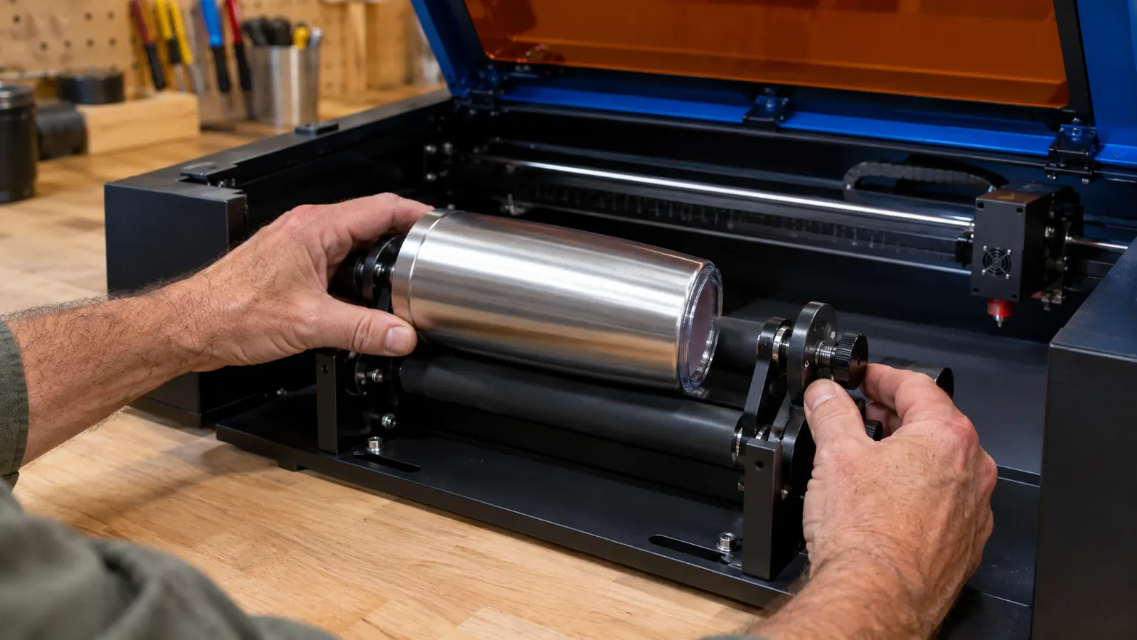Hands adjusting a tumbler between the rollers of a rotary engraving attachment on a laser engraver.